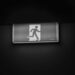Black and white image of an exit sign hung on a plain black wall