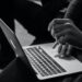 Black and white image of hands typing on a laptop keyboard