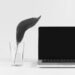 Black and white image of a turned off laptop screen and a glass of water next to it with a large plant leaf shooting out from the glass