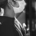 Black and white image of a side-on view of a person wearing a mask and holding a phone to their body