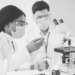 A couple of people in lab coats looking through microscopes
