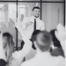 A person in a suit and tie standing in front of a group of people